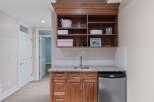 Discover this charming wet bar, perfect for entertaining, featuring a sleek stainless steel mini-fridge and ample storage in the rich wood cabinetry.