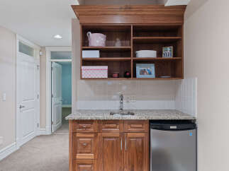 Discover this charming wet bar, perfect for entertaining, featuring a sleek stainless steel mini-fridge and ample storage in the rich wood cabinetry.