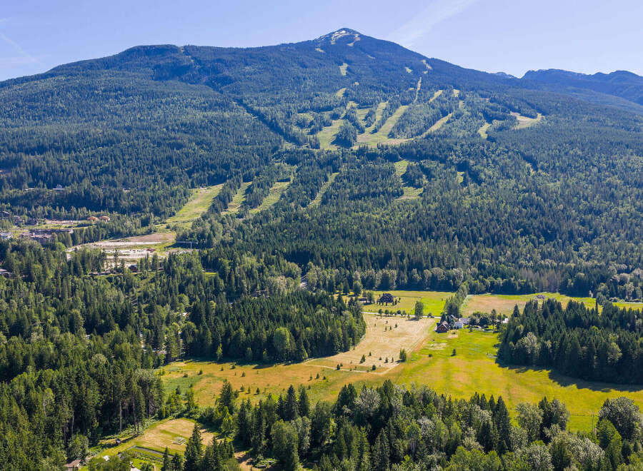 Experience the ultimate mountain lifestyle with this stunning aerial view of a property nestled amidst lush forests and rolling hills.