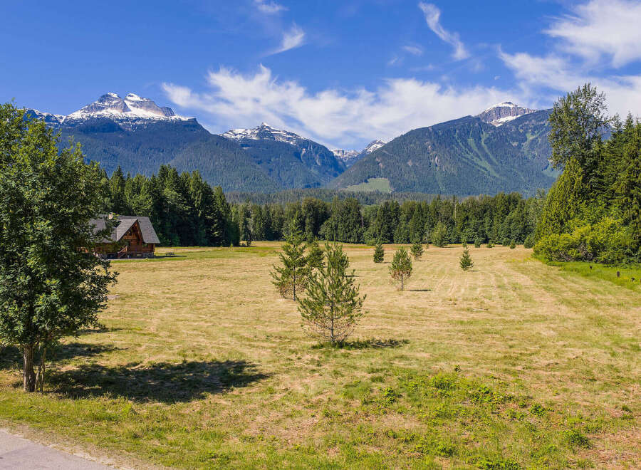 Experience serene mountain living in this picturesque property featuring a charming wooden cabin nestled amidst a vast, sun-drenched meadow.