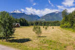 Experience serene mountain living in this picturesque property featuring a charming wooden cabin nestled amidst a vast, sun-drenched meadow.