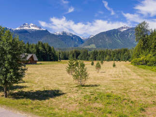 Experience serene mountain living in this picturesque property featuring a charming wooden cabin nestled amidst a vast, sun-drenched meadow.