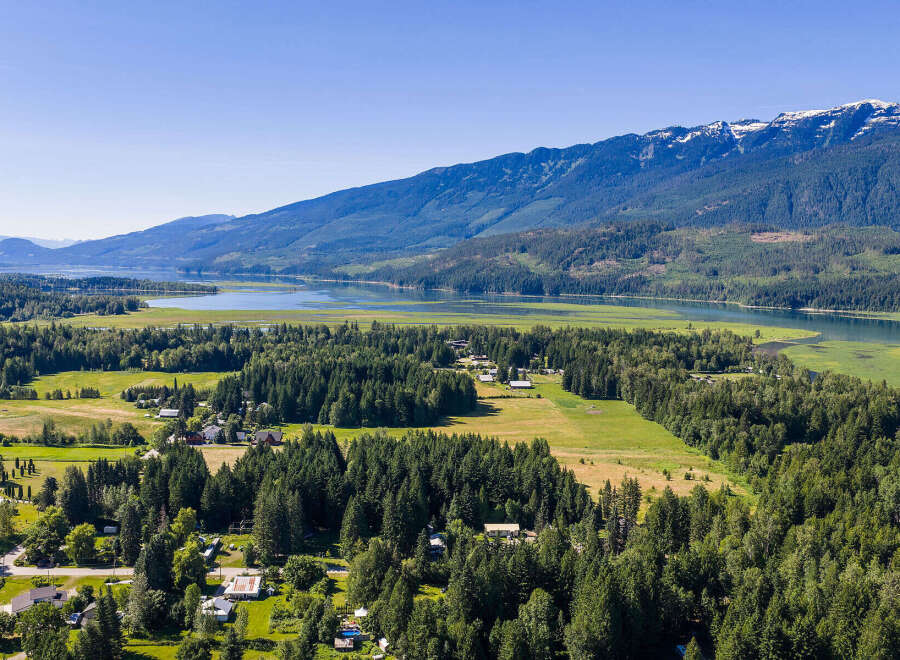 Discover serene living in this picturesque landscape, where lush green fields meet a tranquil lake, all framed by majestic snow-capped mountains.