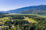 Discover serene living in this picturesque landscape, where lush green fields meet a tranquil lake, all framed by majestic snow-capped mountains.
