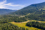 Experience the majestic beauty of this mountain landscape, featuring a sprawling green valley nestled at the foot of towering, tree-covered peaks.