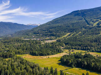 Experience the majestic beauty of this mountain landscape, featuring a sprawling green valley nestled at the foot of towering, tree-covered peaks.