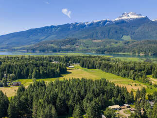 Discover this stunning property nestled amidst lush evergreen forests and rolling green fields, offering breathtaking views of a serene lake and majestic snow-capped mountains.