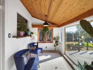 Enjoy abundant natural light and serene views in this charming sunroom, featuring a vaulted wood-paneled ceiling and large windows overlooking the backyard.