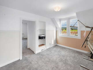 Discover this charming attic room, featuring a unique wavy patterned carpet and a large window offering scenic views of the countryside.