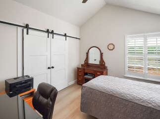 Discover this charming bedroom featuring a stylish barn door leading to a closet, a vintage vanity with a mirror, and a comfortable bed.