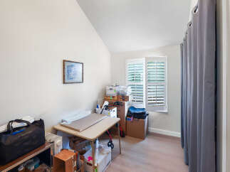 Discover a versatile room perfect for a home office or craft space, featuring a sloped ceiling and ample natural light from plantation shutters.