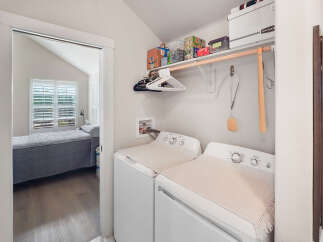 This laundry room features a stacked washer and dryer, ample shelving for storage, and a convenient hanging rod.