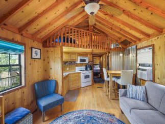 Experience cozy living in this charming cabin featuring a fully equipped kitchen with a stove and microwave, a comfortable living area with a sofa and accent chair, and a dining space.