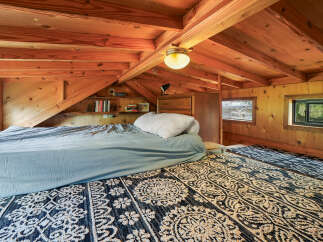 Experience cozy living in this charming loft bedroom, featuring a comfortable bed with light blue linens and a plush white pillow.