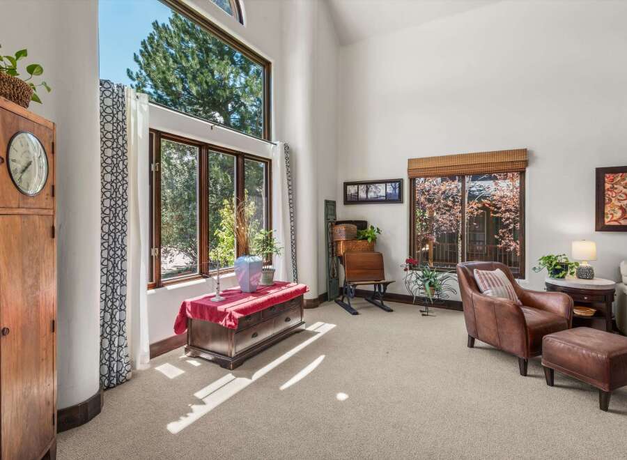 Experience abundant natural light in this living space, highlighted by a soaring vaulted ceiling and expansive windows that frame lush green trees.