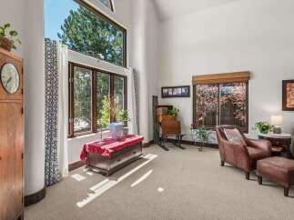 Experience abundant natural light in this living space, highlighted by a soaring vaulted ceiling and expansive windows that frame lush green trees.