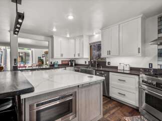 Experience culinary excellence in this stunning modern kitchen, featuring sleek white cabinetry, a spacious quartz island with a built-in microwave, and high-end stainless steel appliances.
