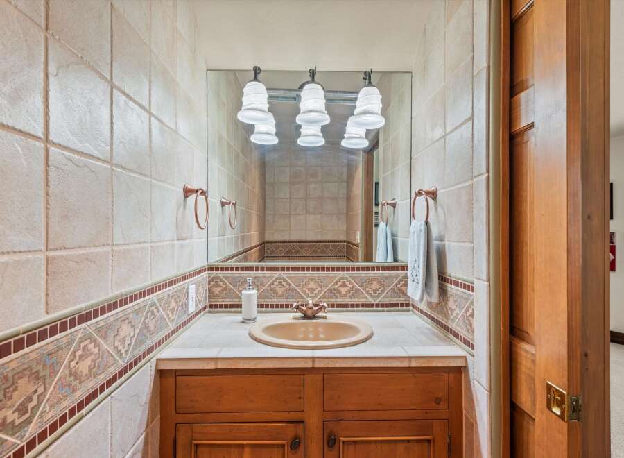 This charming bathroom features a tiled backsplash with a decorative border, a tan sink, and a wooden vanity.