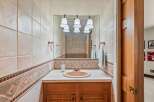 This charming bathroom features a tiled backsplash with a decorative border, a tan sink, and a wooden vanity.