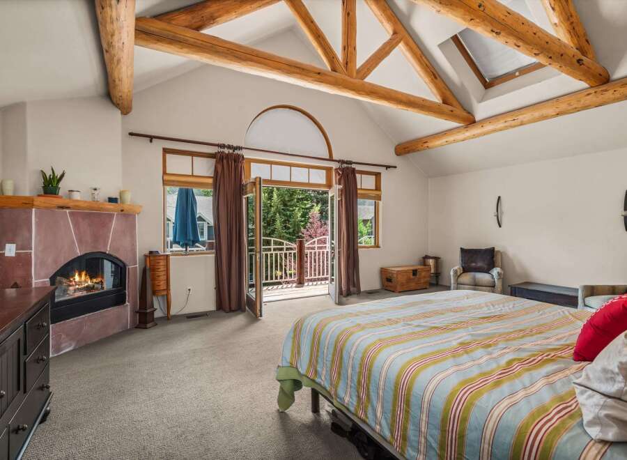 Experience rustic charm in this spacious bedroom featuring a cozy fireplace and vaulted ceilings with exposed wooden beams.