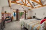 Experience rustic charm in this spacious bedroom featuring a cozy fireplace and vaulted ceilings with exposed wooden beams.