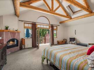 Experience rustic charm in this spacious bedroom featuring a cozy fireplace and vaulted ceilings with exposed wooden beams.