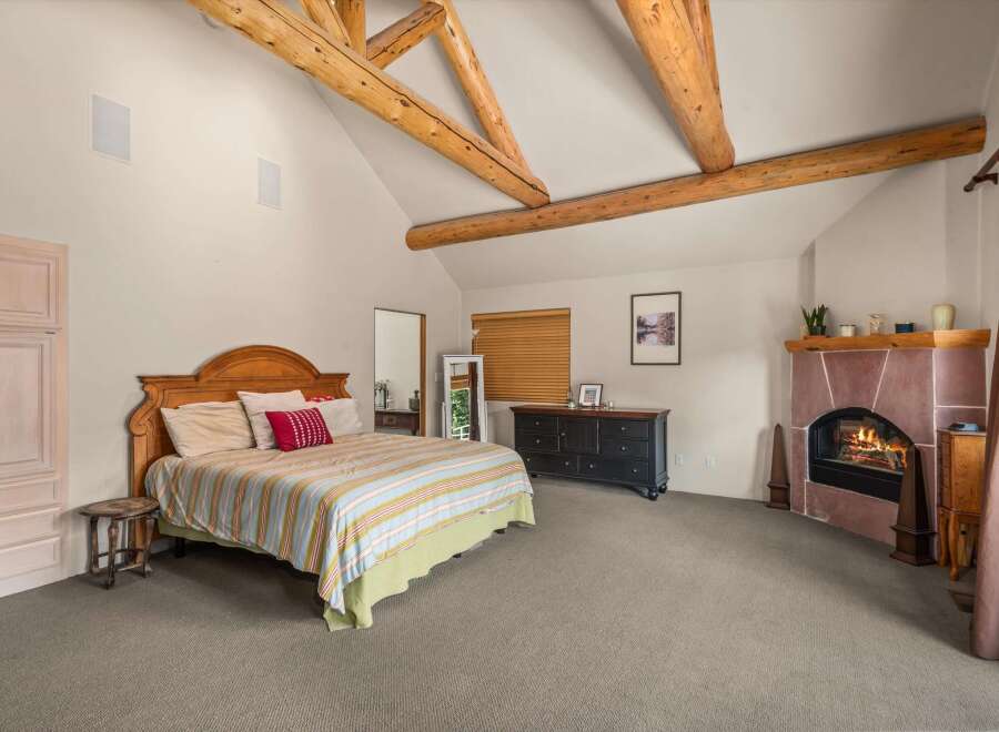 Experience rustic charm in this spacious bedroom featuring exposed wooden beams and a cozy stone fireplace.