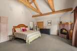 Experience rustic charm in this spacious bedroom featuring exposed wooden beams and a cozy stone fireplace.