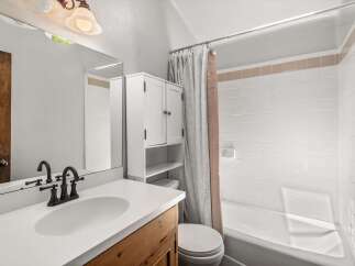 This charming bathroom features a white vanity with a wooden base, complemented by a large mirror and a dark bronze faucet.