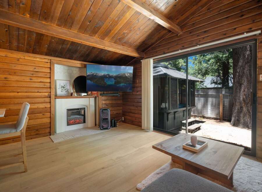 Experience cozy cabin living with this charming interior featuring a modern electric fireplace and a large flat-screen TV mounted on wood-paneled walls.