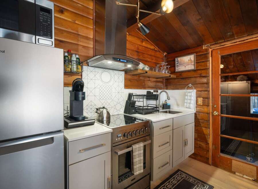 Experience cozy living in this charming cabin kitchen, featuring a sleek stainless steel refrigerator and a modern induction stovetop.