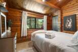 Experience rustic charm in this cozy bedroom featuring warm wood paneling and a vaulted ceiling with exposed beams.