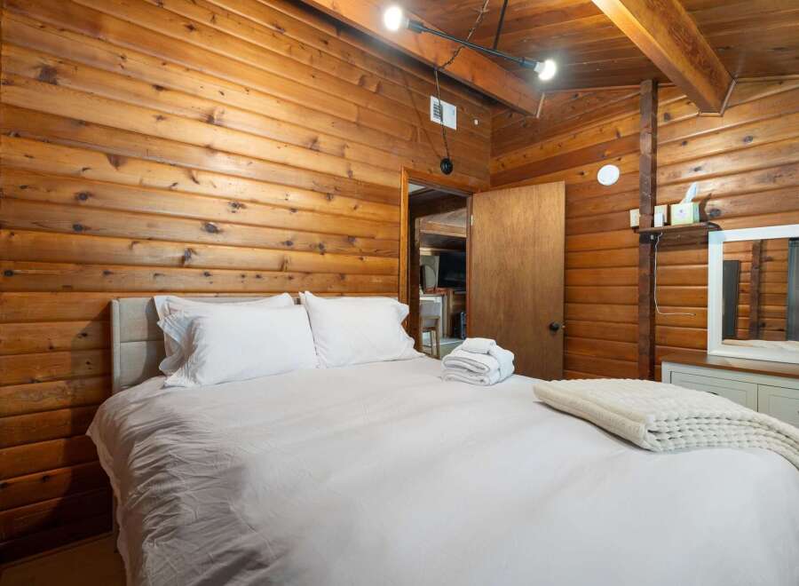 Experience rustic charm in this cozy bedroom, featuring warm wood-paneled walls and a comfortable bed with crisp white linens.