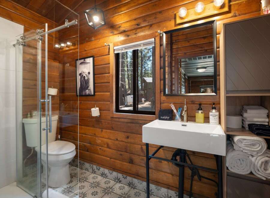 Experience rustic charm in this beautifully appointed bathroom, featuring warm wood paneling and a modern glass shower enclosure.