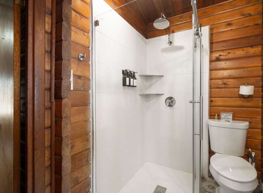 Experience rustic charm in this unique bathroom featuring a modern glass-enclosed shower with multiple dispensers and sleek shelving.