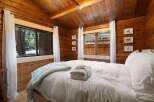 Experience rustic charm in this cozy cabin bedroom, featuring warm wood paneling and a comfortable bed adorned with plush white linens and a light blue throw.