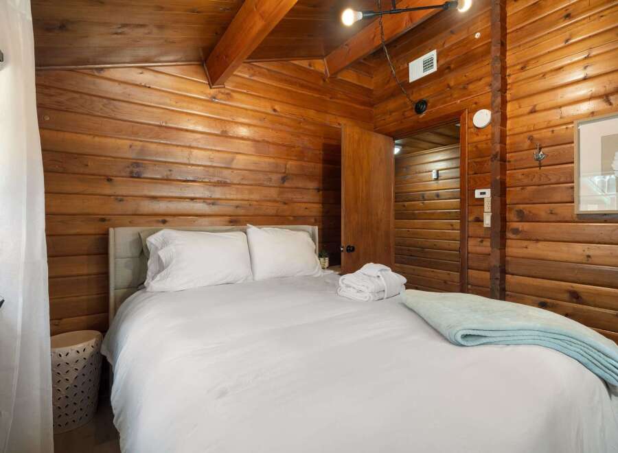 Experience rustic charm in this cozy bedroom featuring warm wood paneling throughout and exposed ceiling beams.