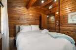 Experience rustic charm in this cozy bedroom featuring warm wood paneling throughout and exposed ceiling beams.