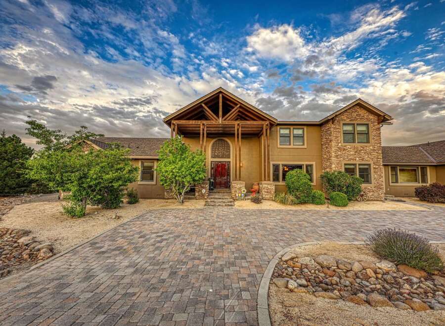 Discover this stunning home featuring a grand entrance with a wooden-beamed porch and a striking red door, perfect for welcoming guests.