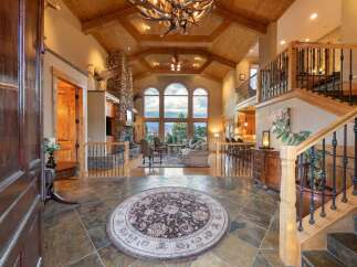 Step into this grand entryway featuring a stunning stone fireplace and vaulted wood-beamed ceilings.