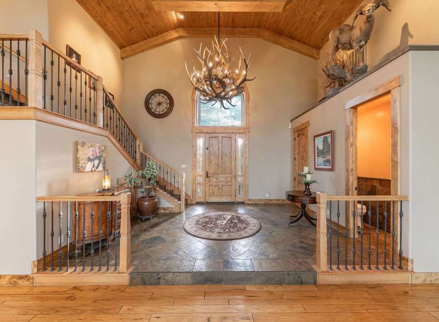 Step into this grand entryway featuring a stunning antler chandelier and a rustic wooden door, complemented by a beautiful slate tile floor and a circular area rug.