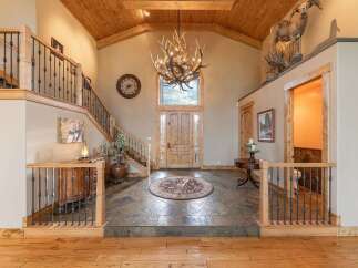 Step into this grand entryway featuring a stunning antler chandelier and a rustic wooden door, complemented by a beautiful slate tile floor and a circular area rug.