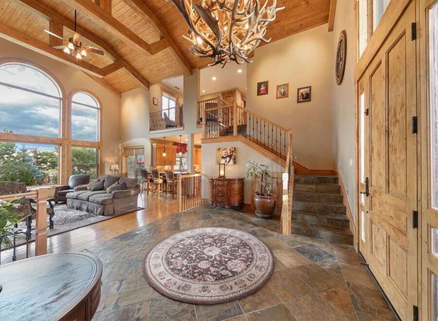 Step into this grand entryway featuring a stunning antler chandelier and soaring vaulted ceilings with exposed wood beams.