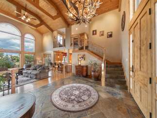 Step into this grand entryway featuring a stunning antler chandelier and soaring vaulted ceilings with exposed wood beams.
