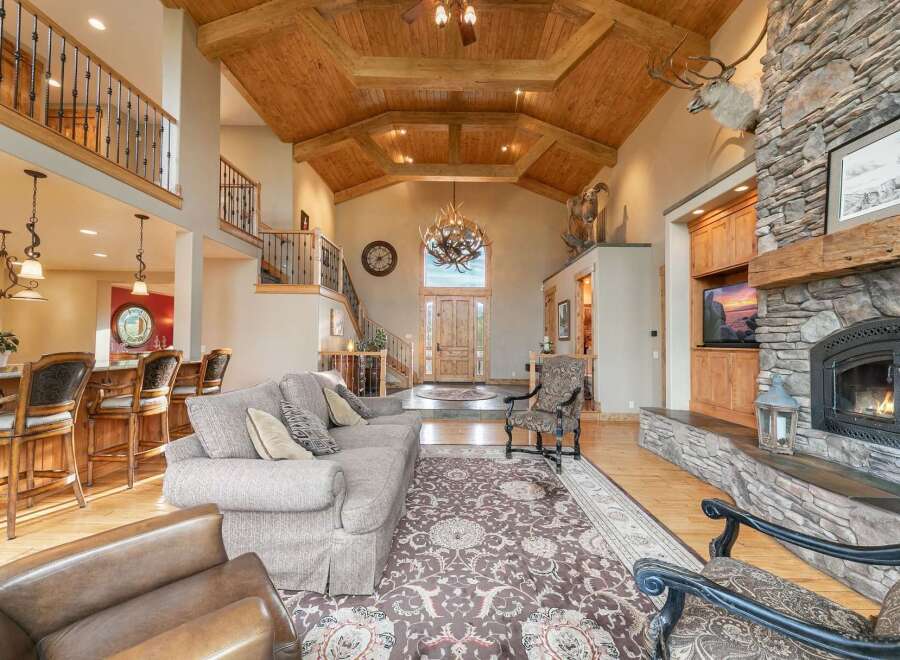 Experience rustic elegance in this grand living room, featuring a soaring vaulted ceiling with exposed wooden beams and a magnificent antler chandelier.