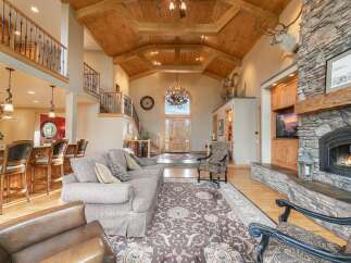 Experience rustic elegance in this grand living room, featuring a soaring vaulted ceiling with exposed wooden beams and a magnificent antler chandelier.