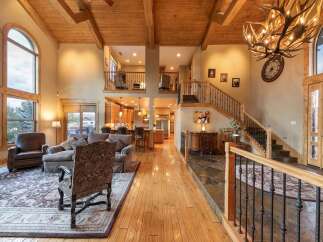 Experience luxurious living in this grand lodge-style home, featuring soaring vaulted ceilings with exposed wooden beams and a stunning antler chandelier.