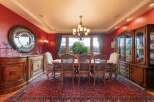 Experience elegant dining in this formal dining room, featuring a stunning red accent wall and a large, ornate rug.