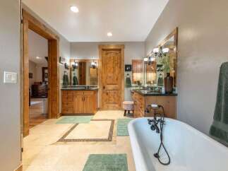 Experience luxury in this spacious bathroom featuring dual vanities with rich wooden cabinetry and granite countertops.