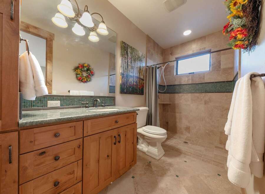 This charming bathroom features a custom wood vanity with a granite countertop, complemented by a tiled backsplash and a large mirror.